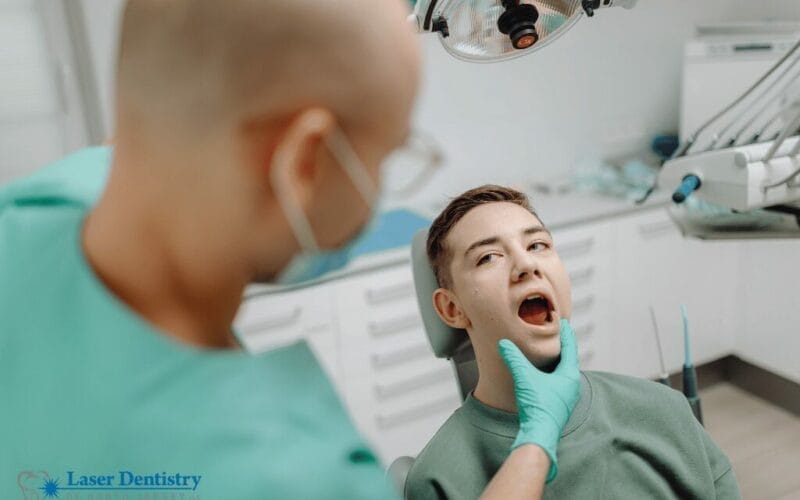 Male dentist examining male patient’s jaw during TMJ evaluation with mouth open